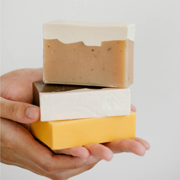 A person holding a stack of three handmade soap bars.